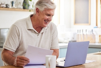 An older man sits in front of a laptop