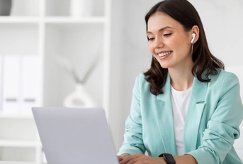 A woman typing on her computer and wearing a set of earbuds. 