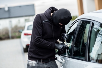 thief breaking car window using screwdriver