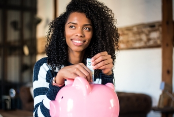 Smiling woman putting money in a piggy bank