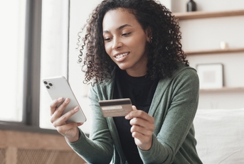 Woman looking at her phone and holding a credit card