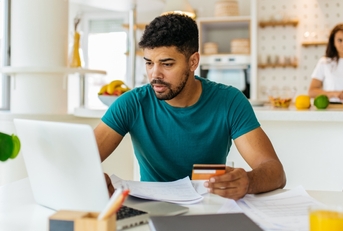 Man holding a credit card and looking at a laptop