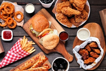 Table scene of assorted take out or delivery foods. Hamburgers, pizza, fried chicken and sides. Top down view on a dark wood banner background.