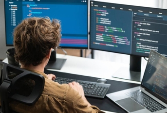  man working from home on pc monitors at modern home office doing coding
