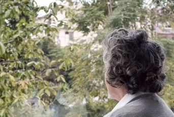 elderly woman looking out window longingly