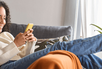 Smiling woman sitting on a couch and using a phone