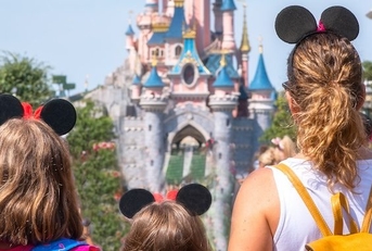 A mother and her daughters gaze at the Princess Castle in a Disney park.