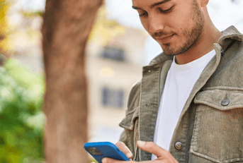 A young person looks down at their phone while standing outside.