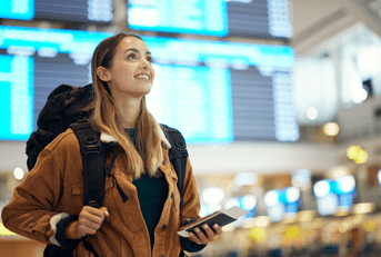 A woman wears a backpack and holds her phone in the middle of an airport.