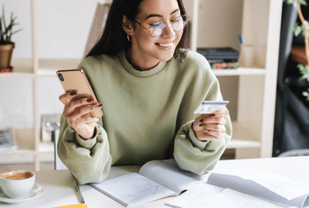 A woman smiles as she holds her phone and a credit card. 