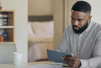 A man is looking at his tablet at the kitchen counter. 