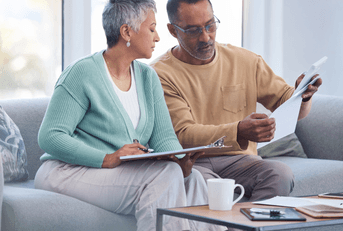 A man and woman look over insurance papers together on a couch.