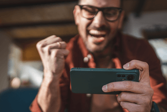A man cheers while playing a game on his phone.