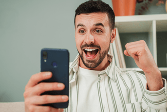 A man cheers while playing a game on his phone.