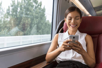 A woman smiles while playing on her phone on a train.