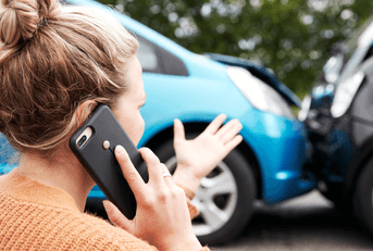 A woman talks on her phone in front of a fender bender.