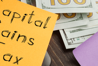 Capital gains tax written on a post-it note next to money