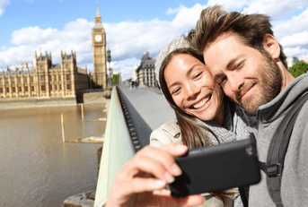 A woman and man smile together on a bridge while taking a picture.