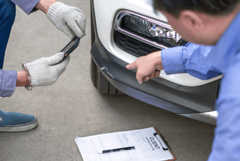 Two individuals inspect damage on a vehicle