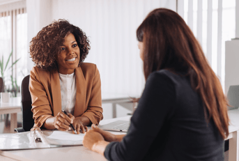 Two women are speaking to each other at a bank.