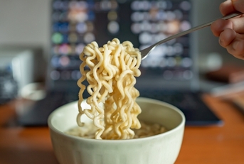man eating ramen with laptop at work
