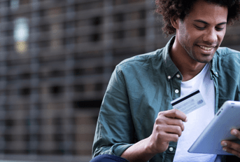 A smiling man holds a credit card and tablet.