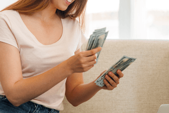 A woman counts a stack of cash on her couch.