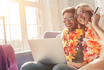 A man and woman wear leis and use a laptop to book their tickets.