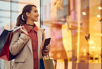 A woman shopper holds shopping bags and passes by a storefront. 