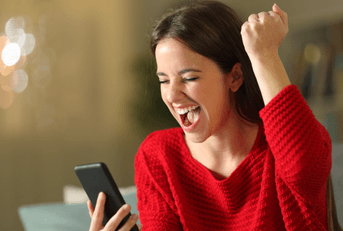 An excited woman raises her first as she plays a game on her phone.