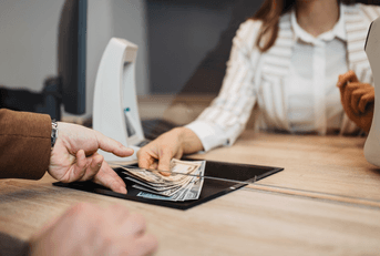 A bank teller hands cash to a customer through a window. 