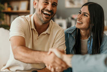 A man shakes hands with someone while his spouse smiles up at him.