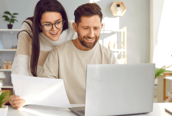 A man uses a laptop while a woman peers over his shoulder.