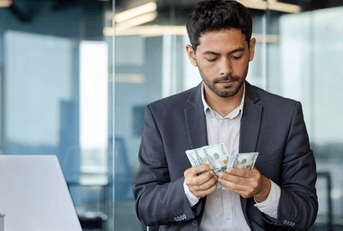 A man counts his cash while sitting in front of his laptop at the office.