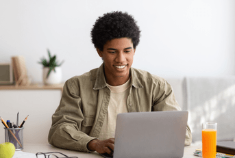 A man smiles while using his laptop at home.