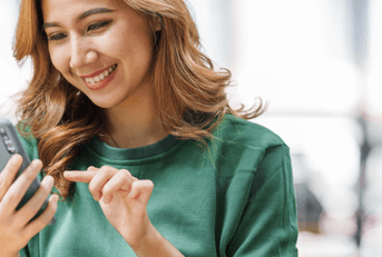 A woman in a green sweater smiles while using her phone. 