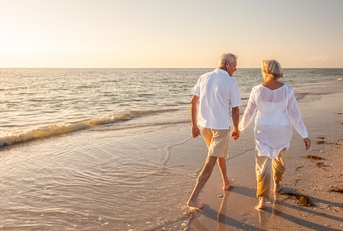 retired couple walking holding hands on beach