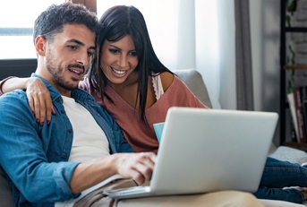 Couple sitting together on couch and looking at computer screen together