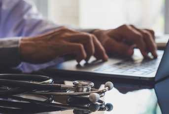 male doctor typing on laptop with medical stethoscope on the desk