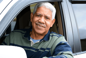 A senior rests his elbow out of his car's window and smiles at the camera. 