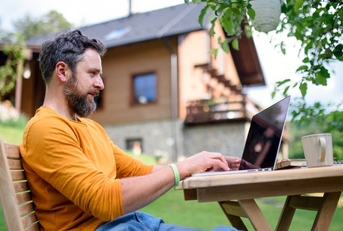 Side view of man with laptop working outdoors in garden, home office concept