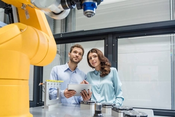 Colleagues in high tech company controlling industrial robots, using digital tablet