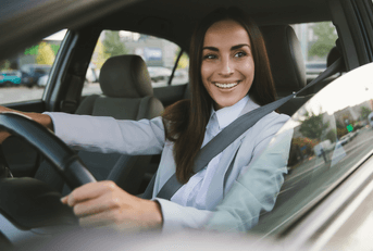 A woman in a suit smiles while she drivers her car.