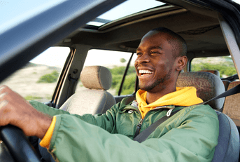 A man in a green jacket smiles and laughs as he grips the steering wheel.