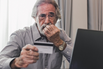 upset senior man holding credit card