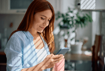 Smiling woman looking at her phone and holding a mug