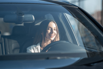 A woman smiles while driving her car.