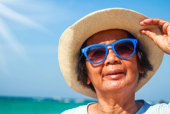 woman enjoys fun, visiting the sea, wearing a hat and wearing blue sunglasses