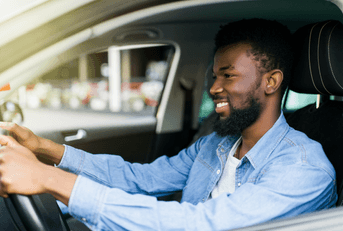A young man in a blue button down grips the wheel and smiles.