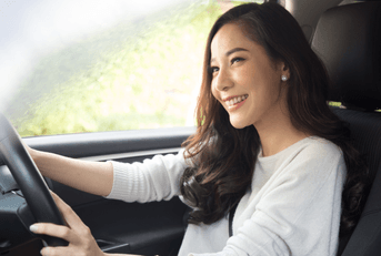 A woman with long brown hair smiles while driving her car.